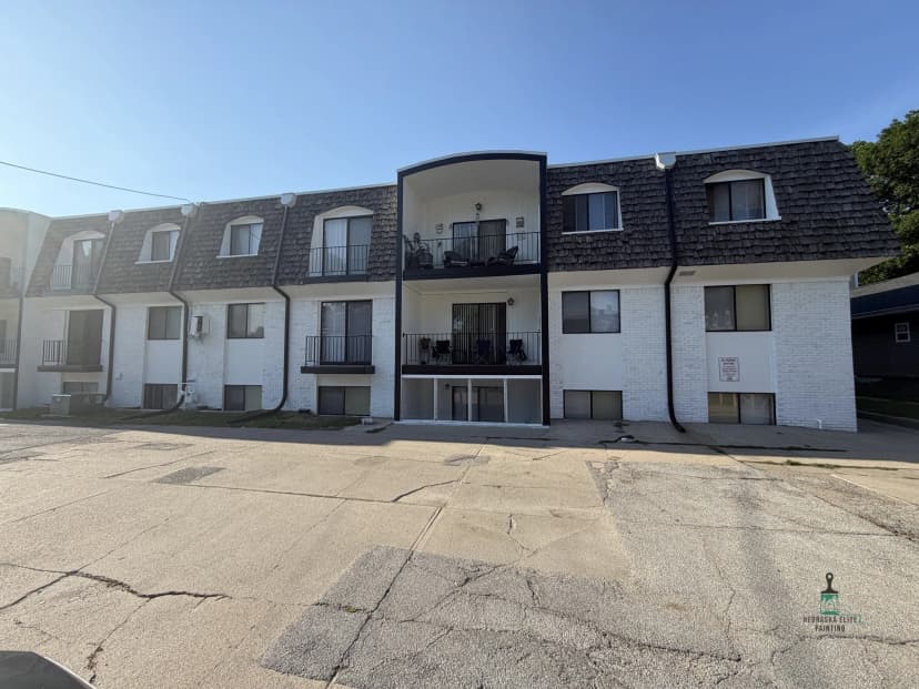 Two-story apartment building with white exterior and black accents under clear blue sky.