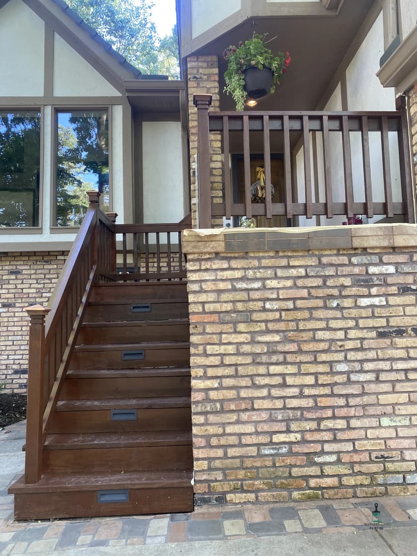 Wooden stairs leading to a brick entryway with a balcony and potted plants.