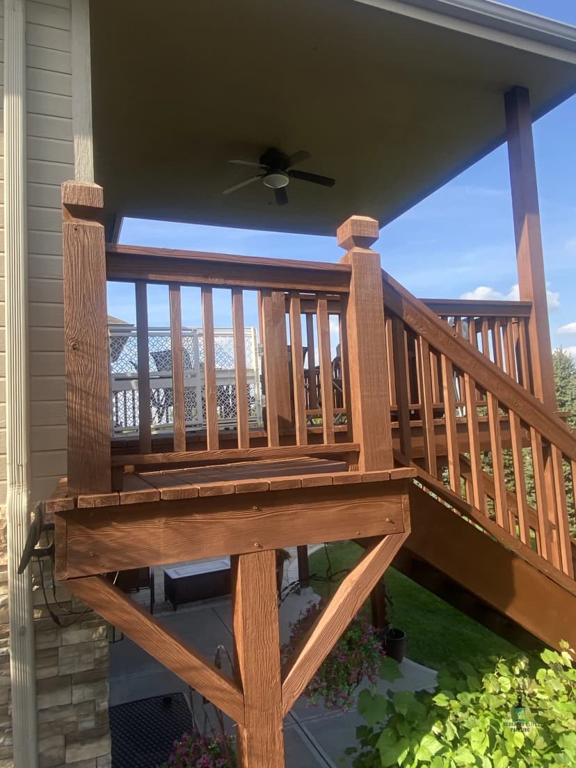 Wooden deck with railing and stairs, featuring a ceiling fan and landscaped yard.