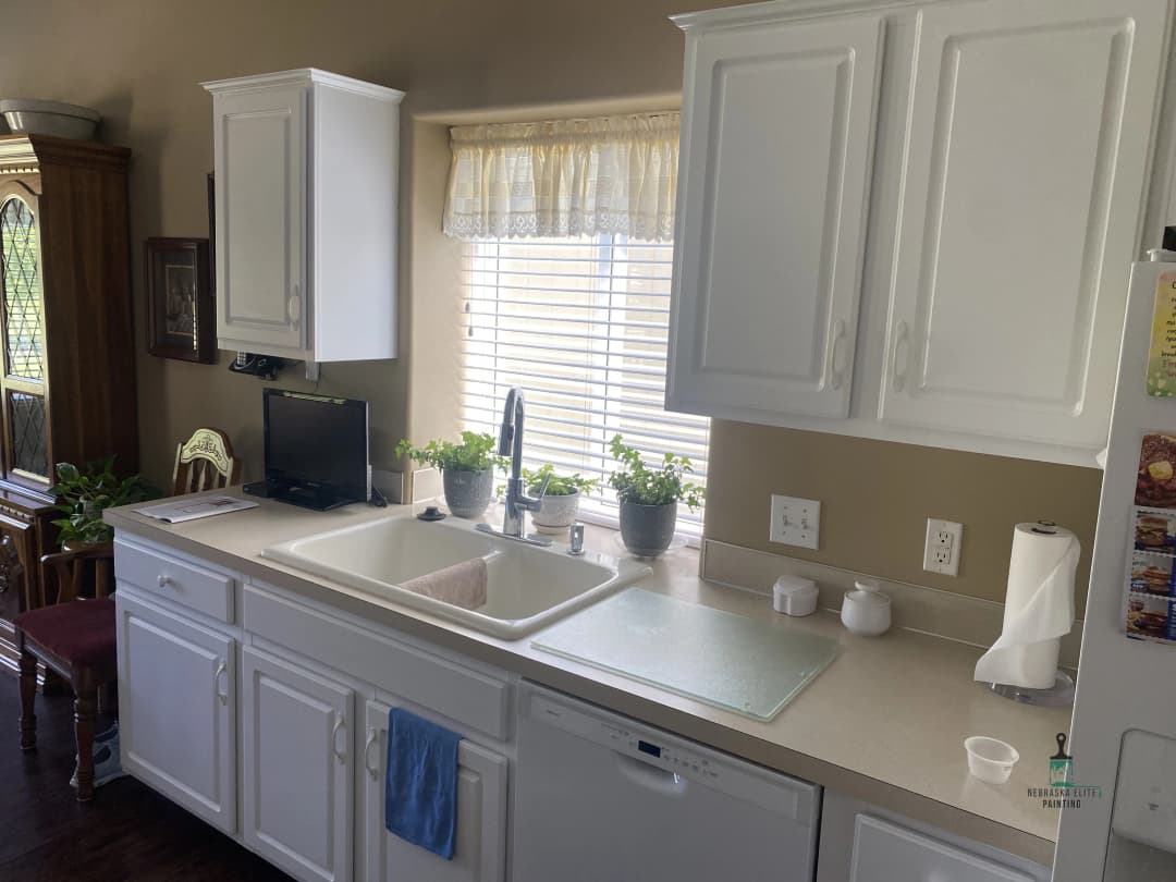 Bright kitchen with white cabinets, sink, plants, and window for natural light.