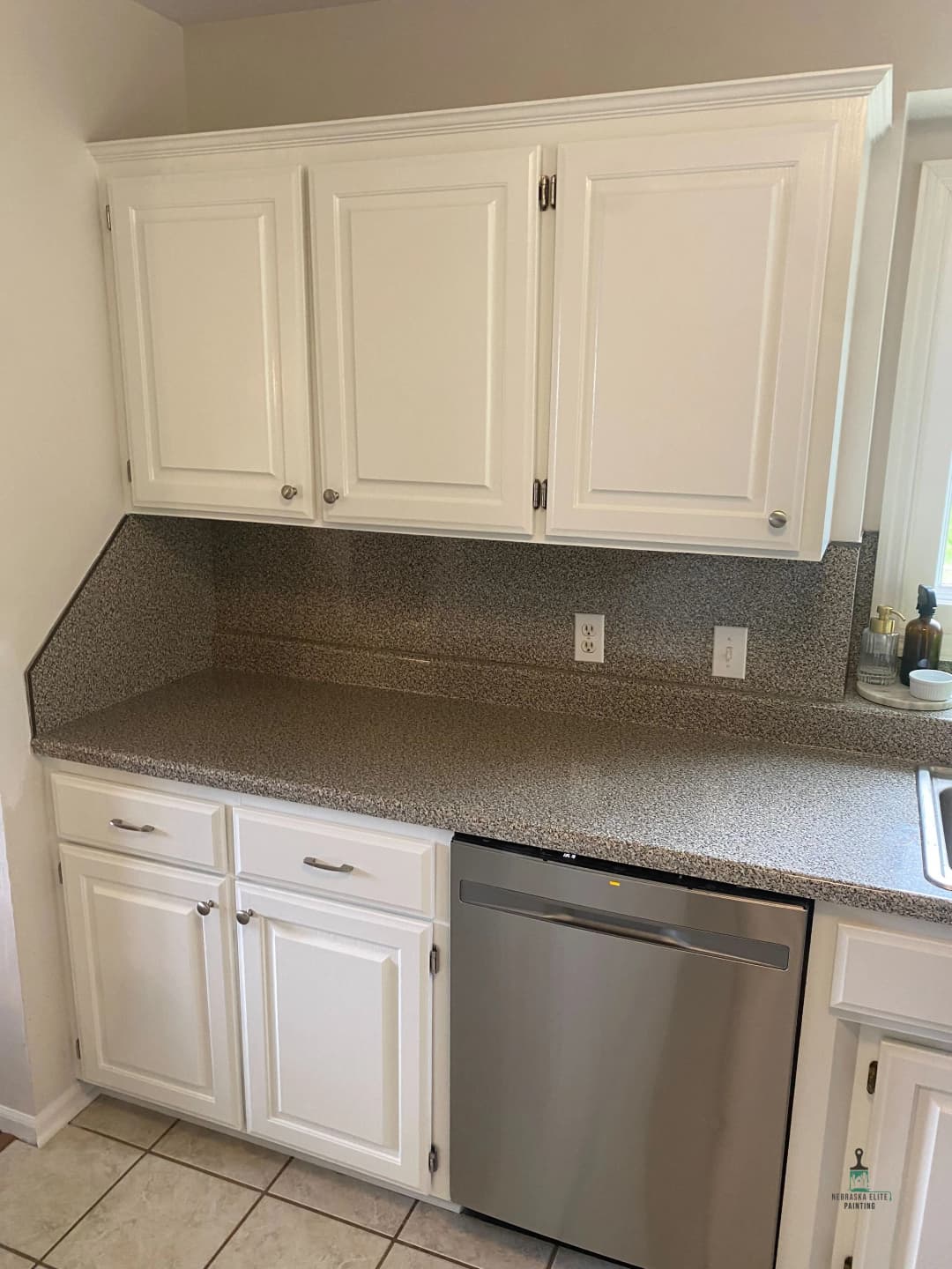 Modern kitchen with white cabinets, stainless steel dishwasher, and speckled countertop.