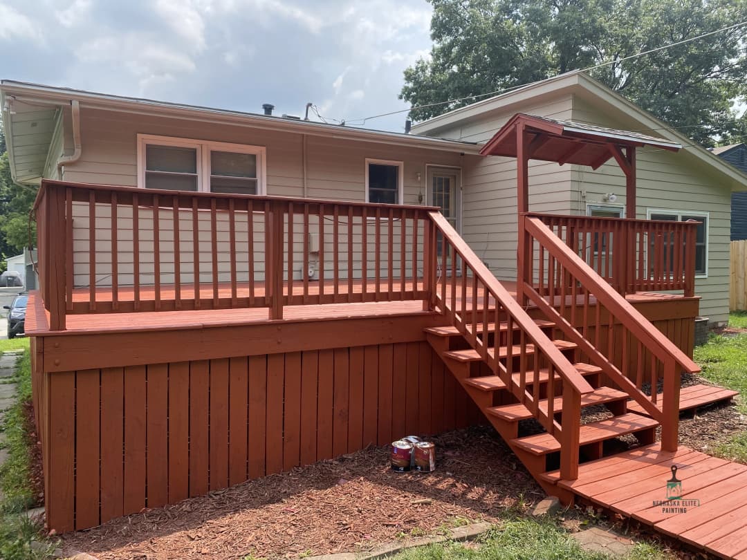 Freshly stained wooden deck with stairs leading to a house, surrounded by green grass.