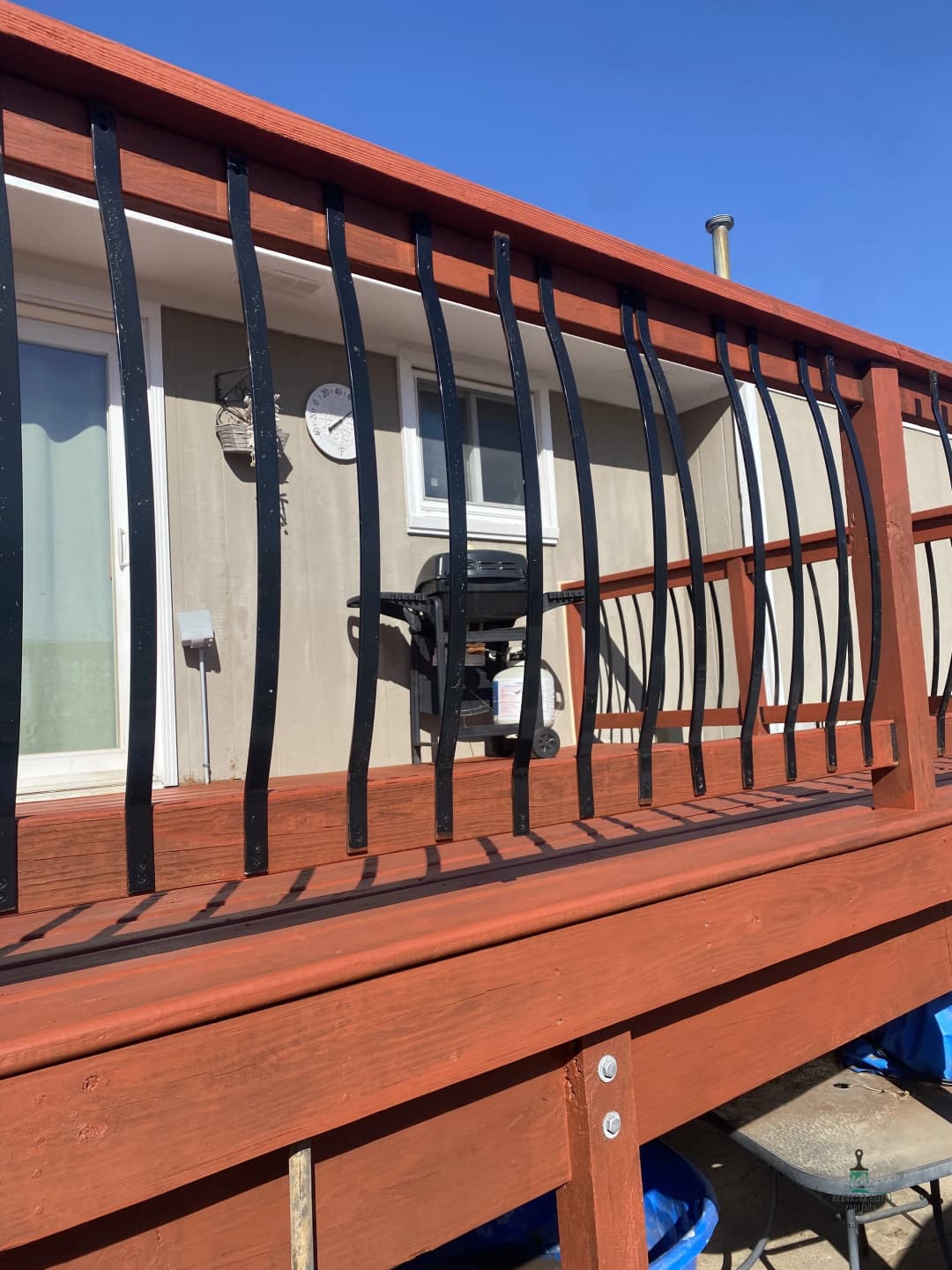 Wooden deck railing with curved black metal bars, outdoor grill visible in the background.