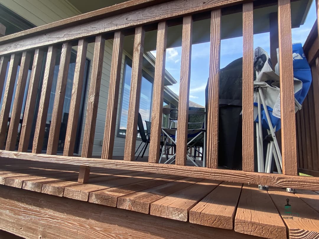Wooden deck railing with furniture and mountains visible in the background. Sunny day.