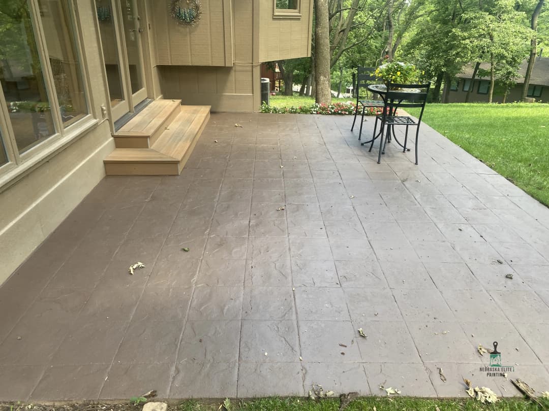 Paved patio area with steps, table, and chairs surrounded by greenery.