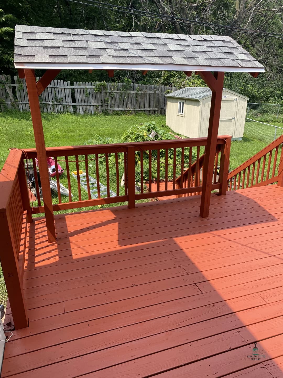 Wooden deck with a gabled roof overhang, grassy yard, and garden shed in the background.