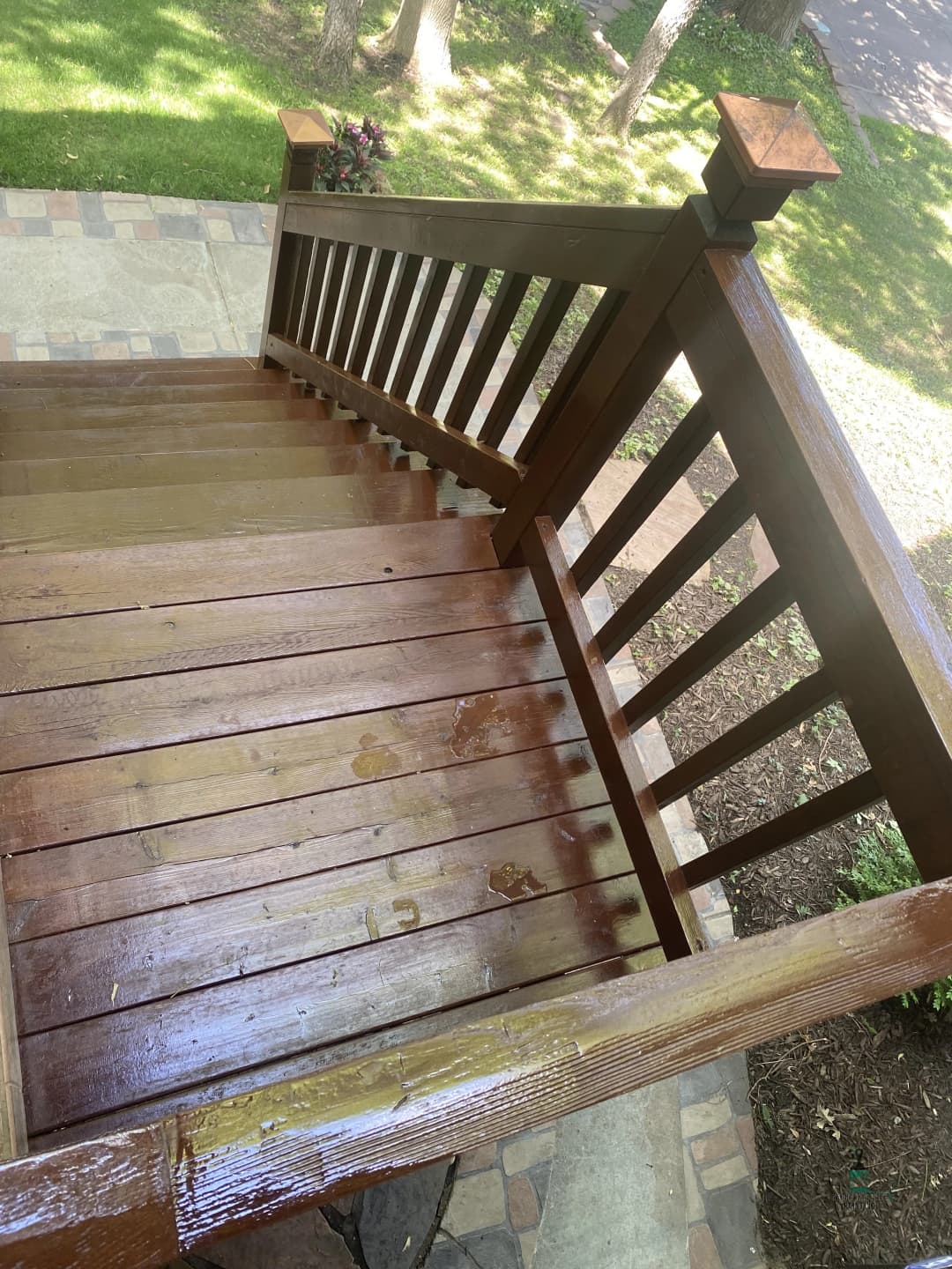 Wooden stairs with a polished railing, surrounded by greenery and stone pathway.
