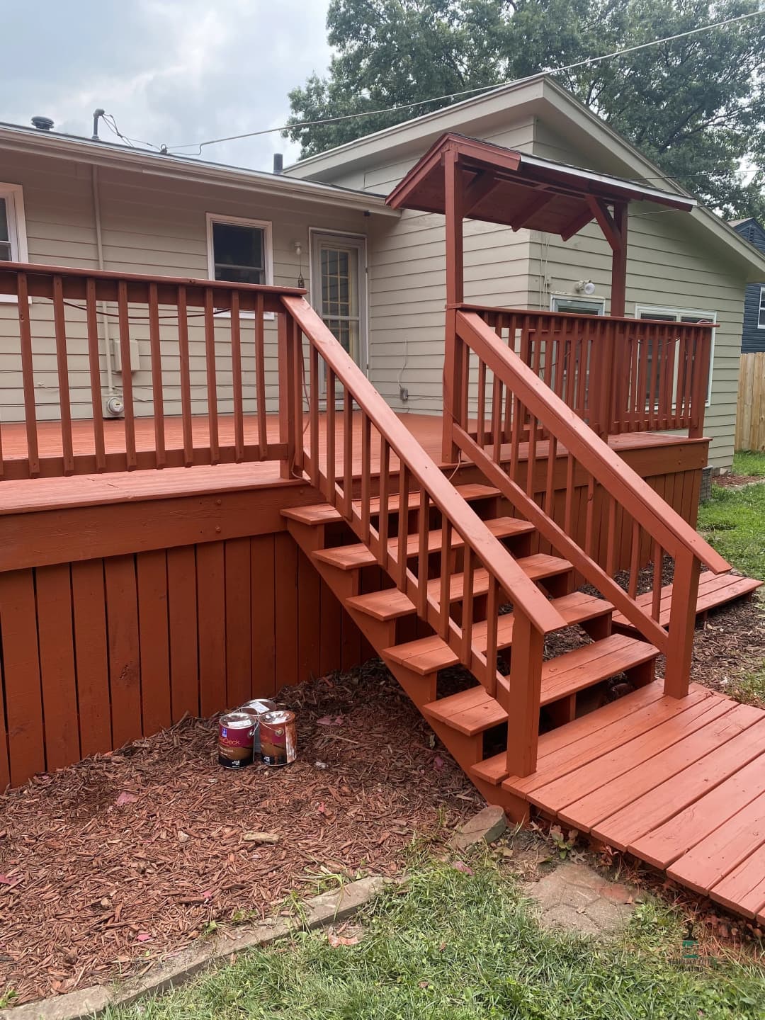 Newly painted red wooden deck with stairs and a covered entryway in a residential backyard.