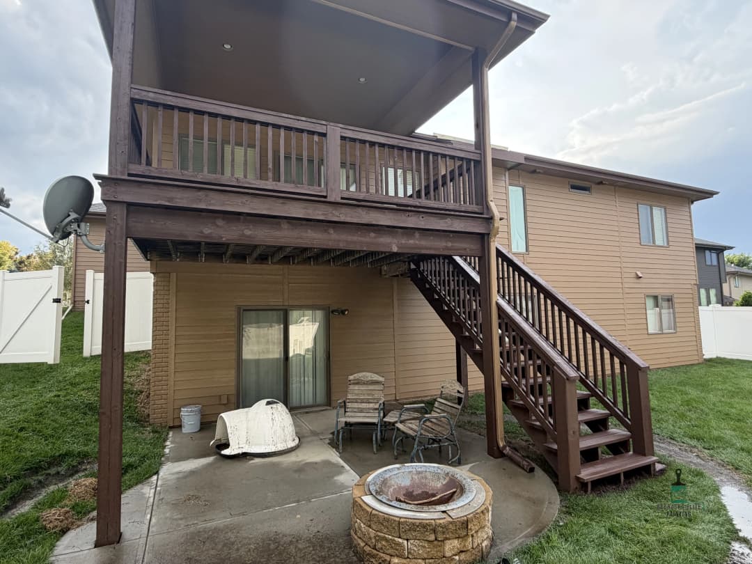 Backyard view of a multi-level home with a wooden deck, staircase, and seating area.
