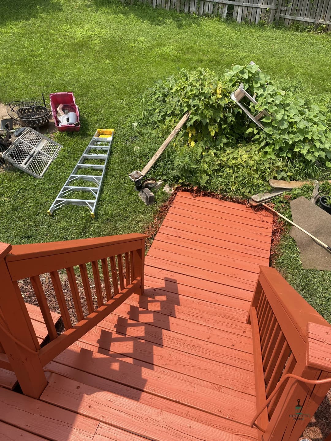 View from above red wooden stairs leading to a garden and gardening tools in a backyard.