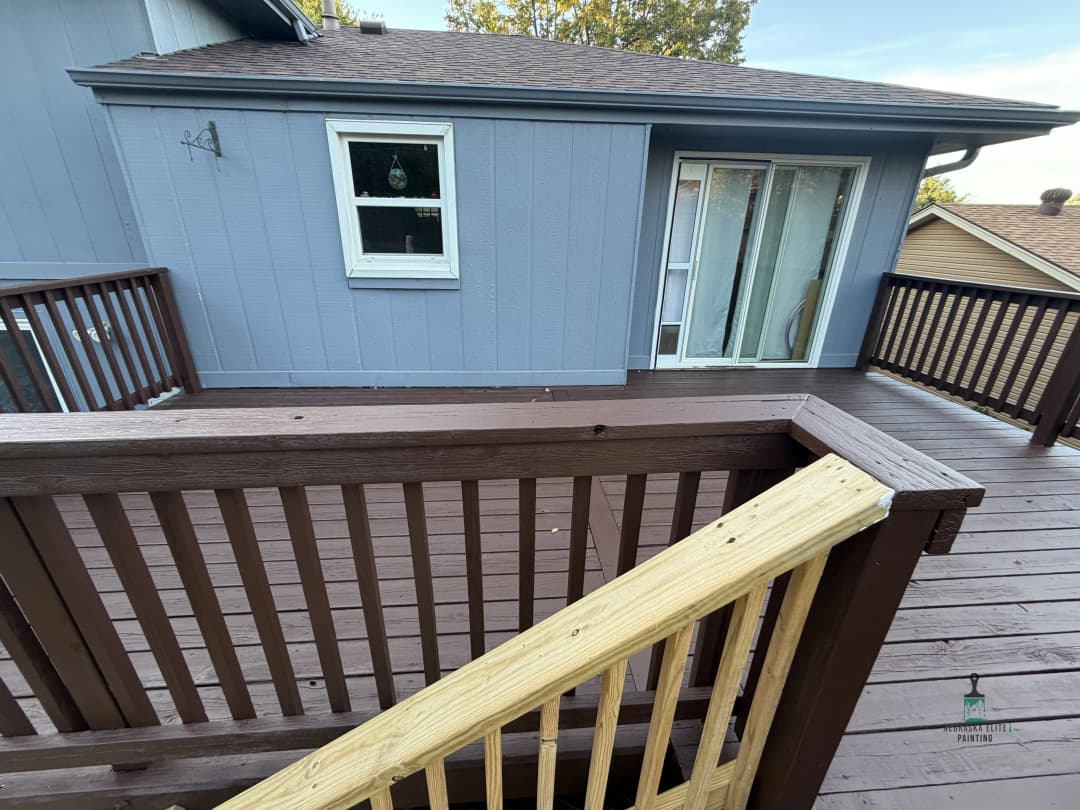 Exterior view of a wooden deck with railings and access to a light blue house.