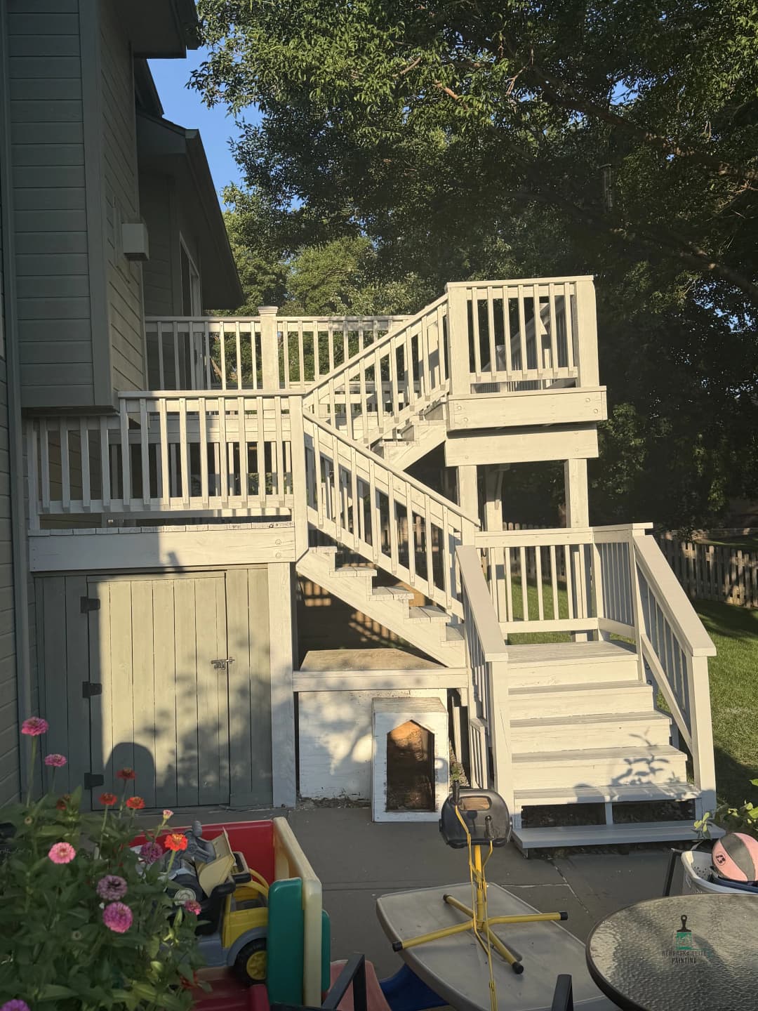 Exterior wooden staircase with multiple levels leading to a house, surrounded by greenery.