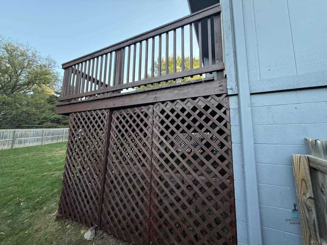 Wooden deck with lattice railing and green grass in backyard. Home exterior view.