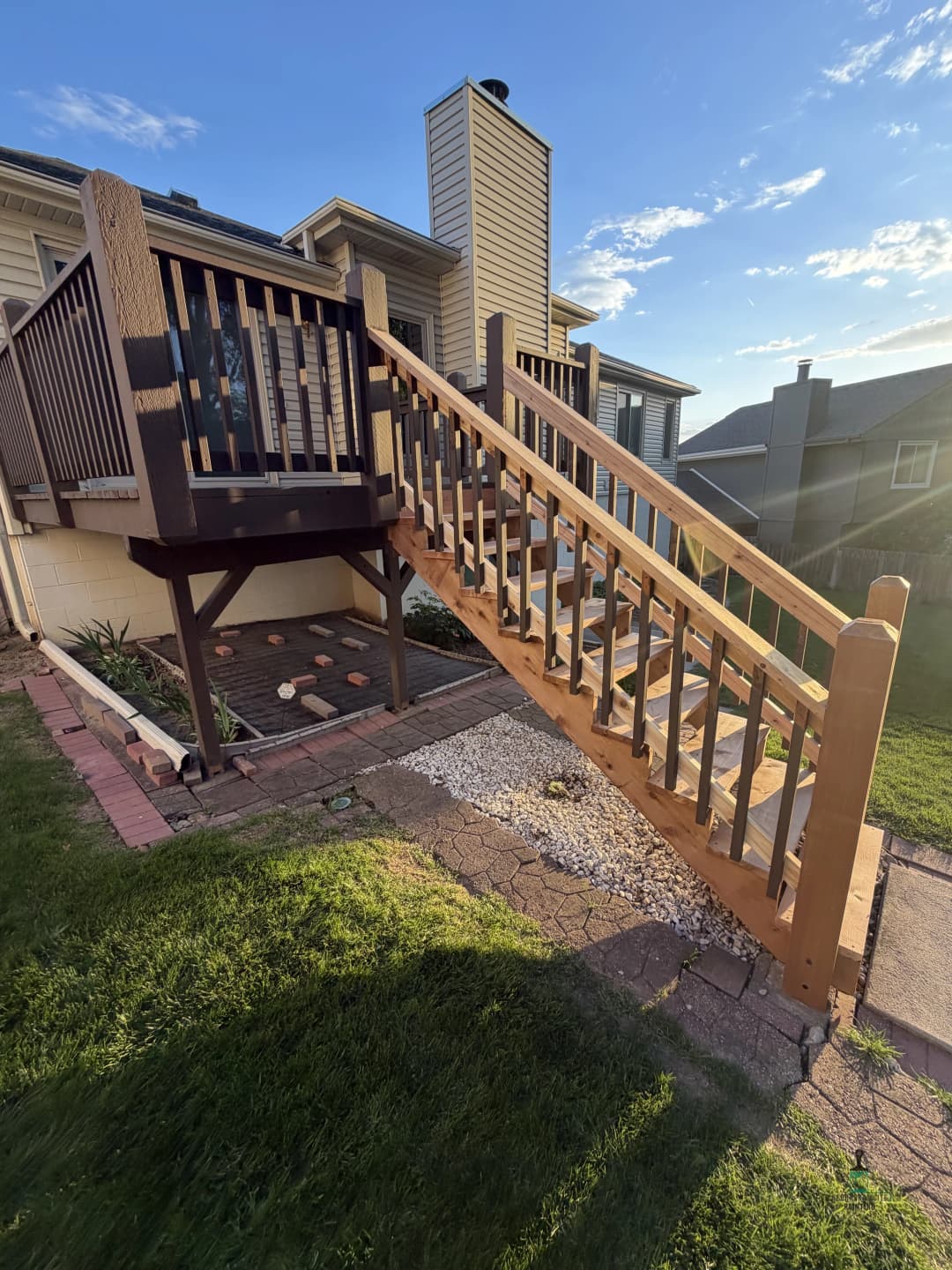 Wooden staircase leading to a house, surrounded by a landscaped yard and blue sky.