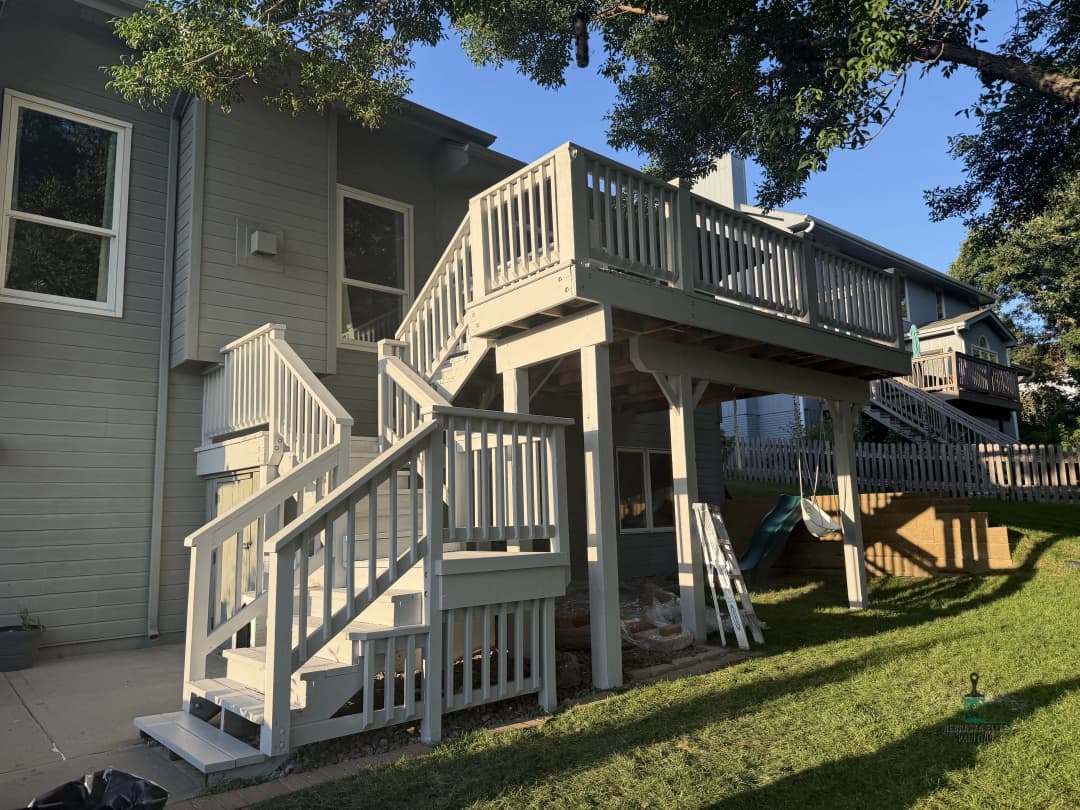 Two-story wooden deck with stairs in a residential backyard.
