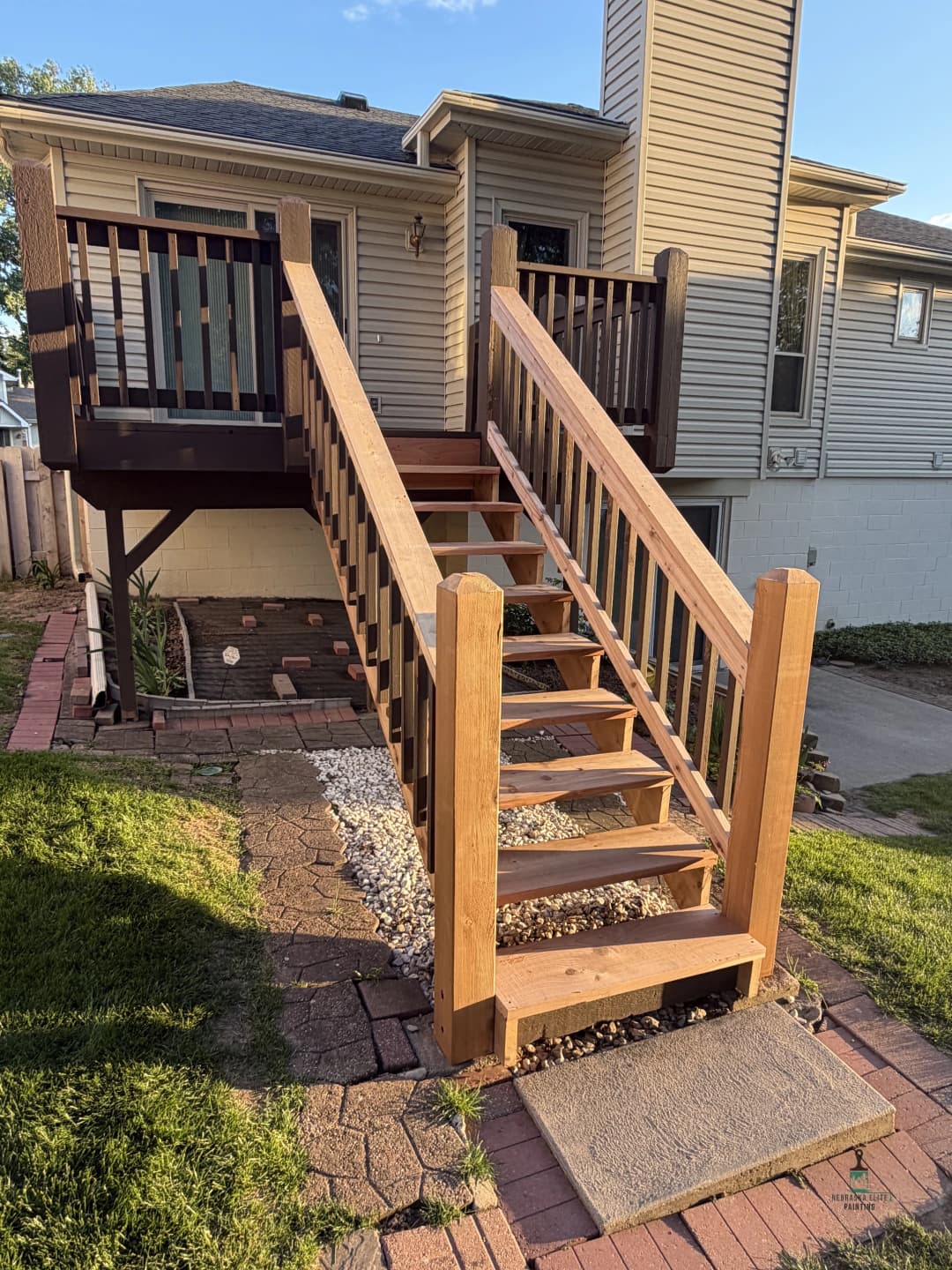 Wooden stairs leading to a house with a landscaped yard and brick walkway.