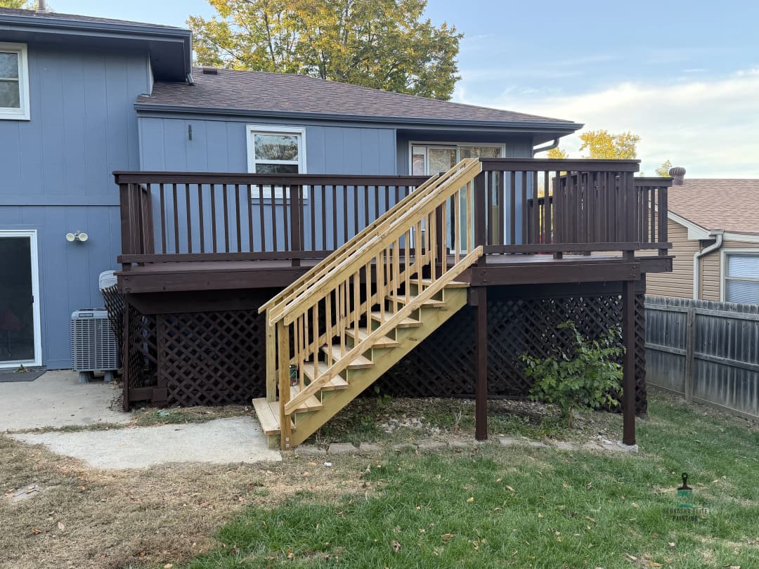 Exterior view of a wooden deck with stairs attached to a blue house in a residential area.