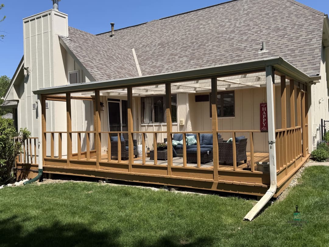 Wooden deck with screened enclosure and seating, surrounded by a green lawn and clear blue sky.