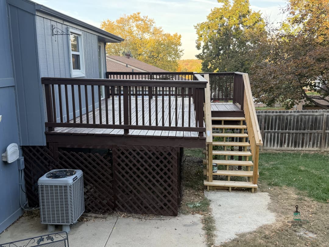 Wooden deck with stairs, surrounded by trees and lawn, featuring an air conditioning unit nearby.