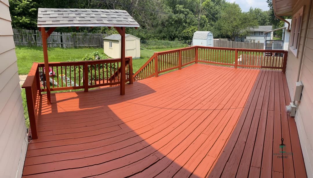 Spacious red wooden deck with gazebo and green backyard, ideal for outdoor living.
