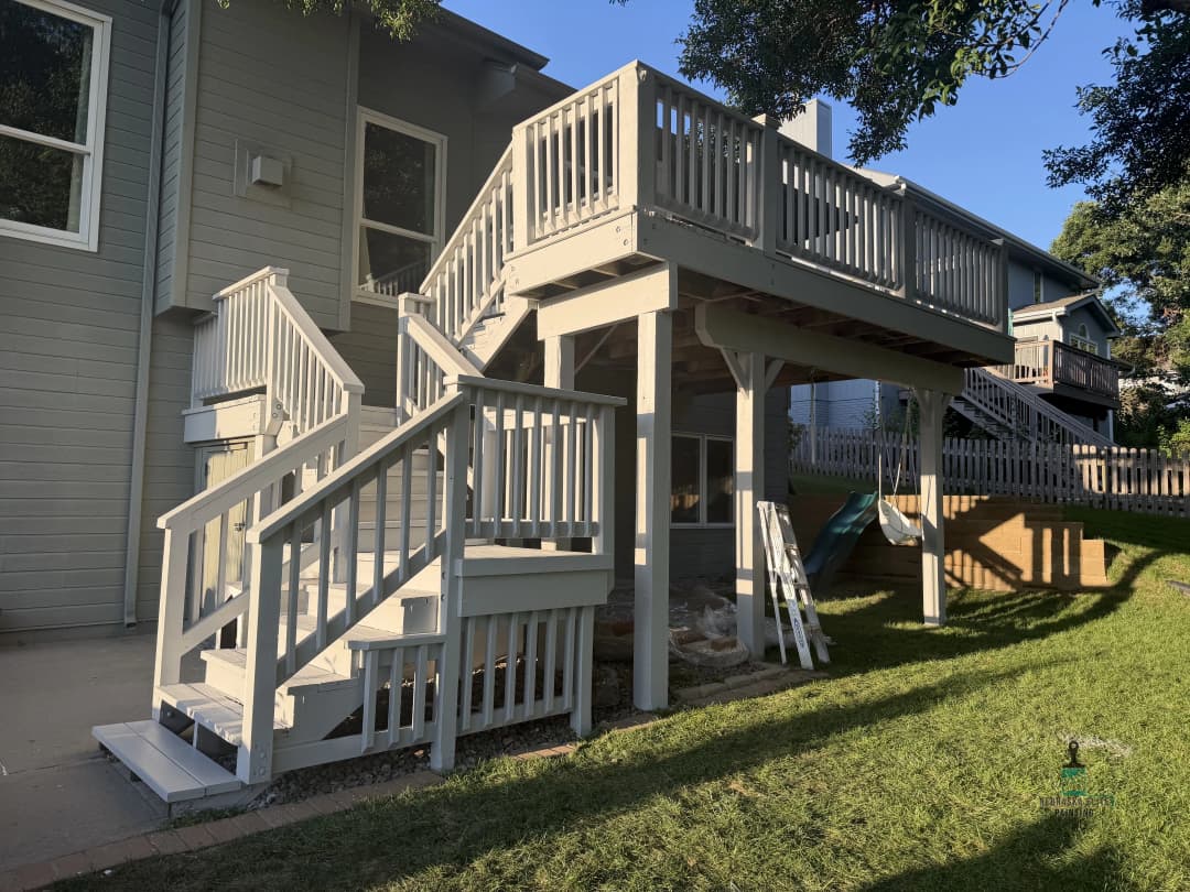 White wooden deck and stairs in a backyard setting with green grass and houses nearby.