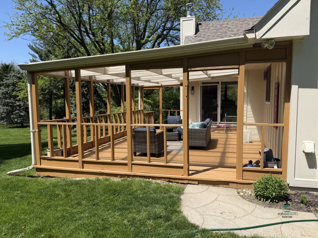 Modern screened porch with wicker furniture and wooden deck, surrounded by greenery.