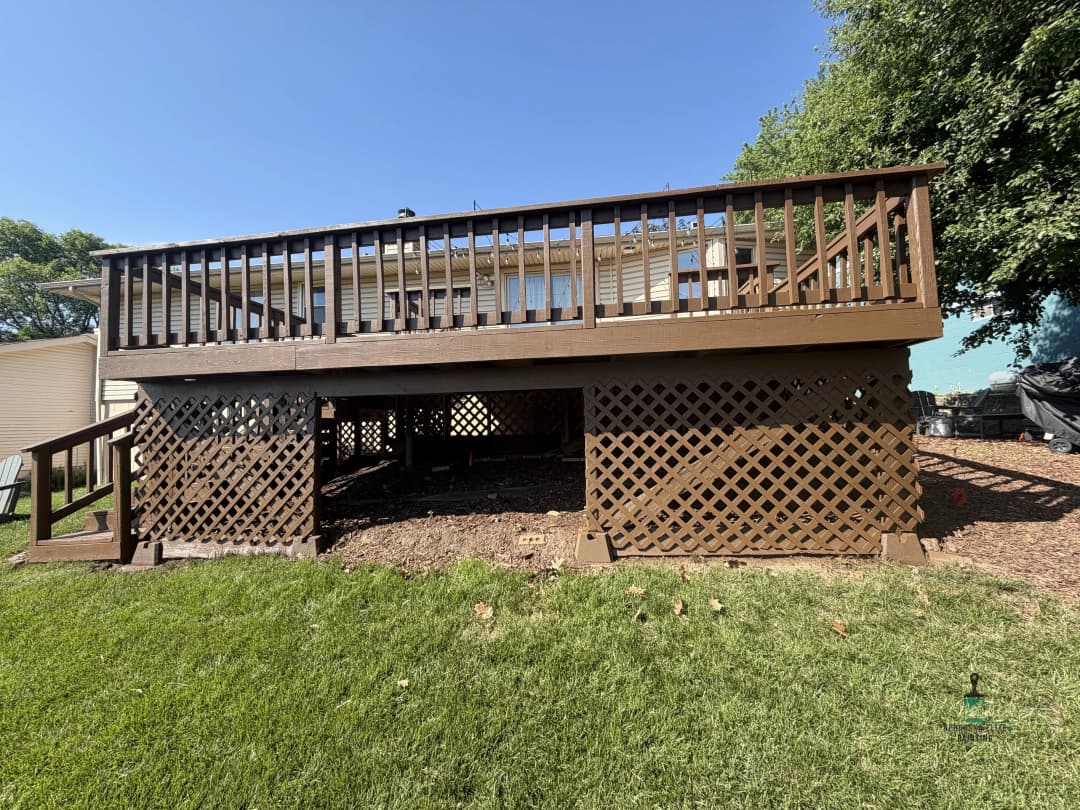 Brown wooden deck with lattice skirting, surrounded by green grass and trees.