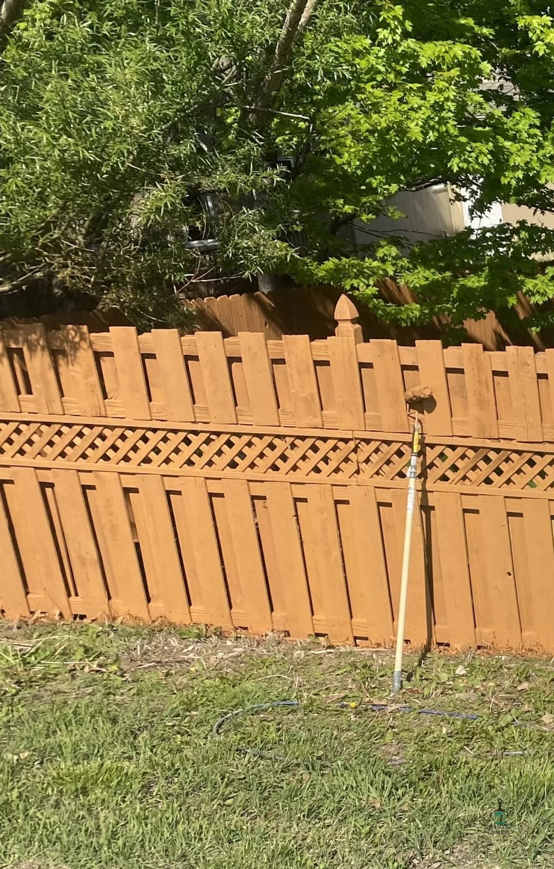 Wooden fence with a decorative lattice design and a paint roller leaning against it.