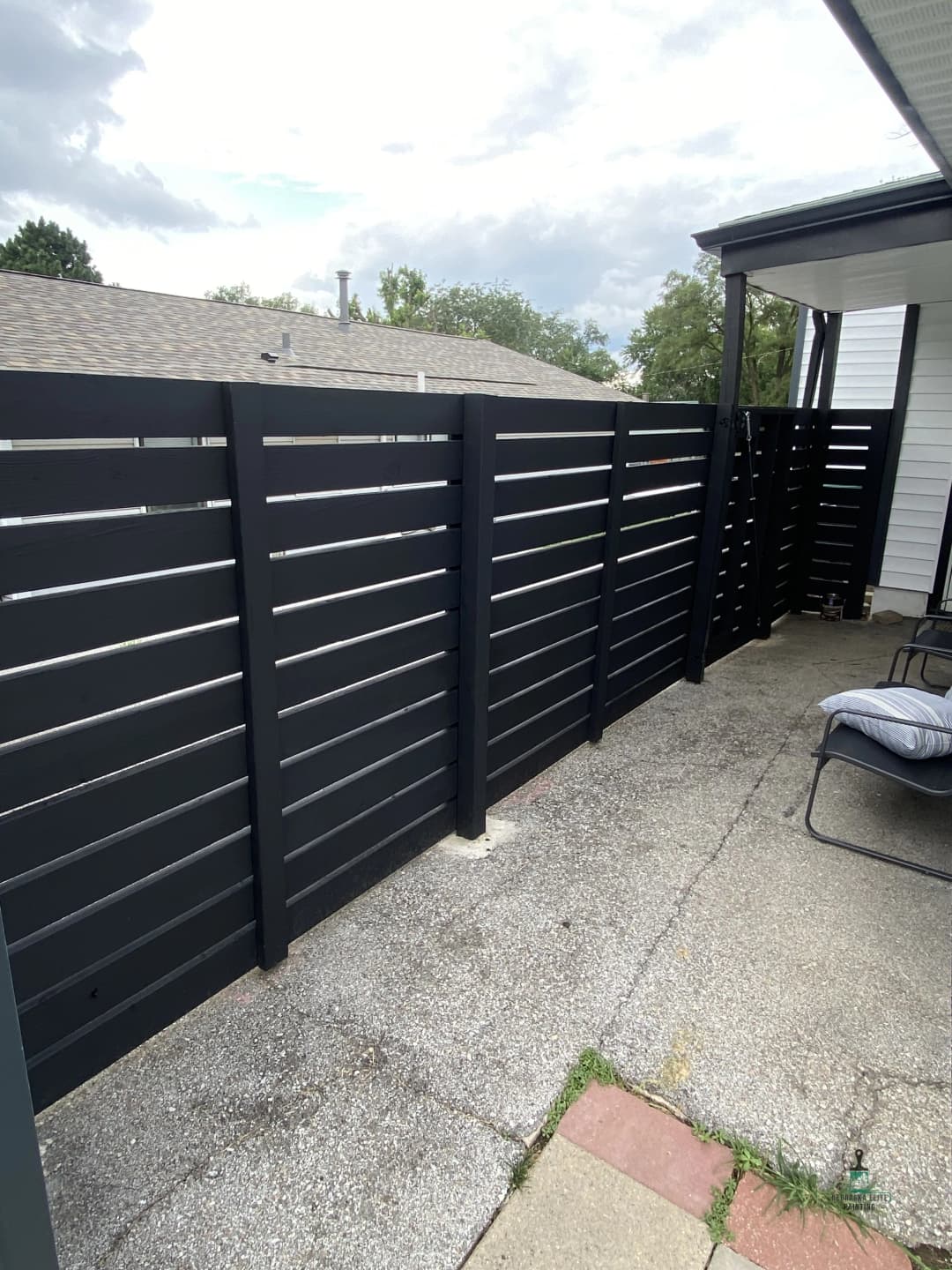 Modern black horizontal slat fence creating a private outdoor space with concrete flooring.