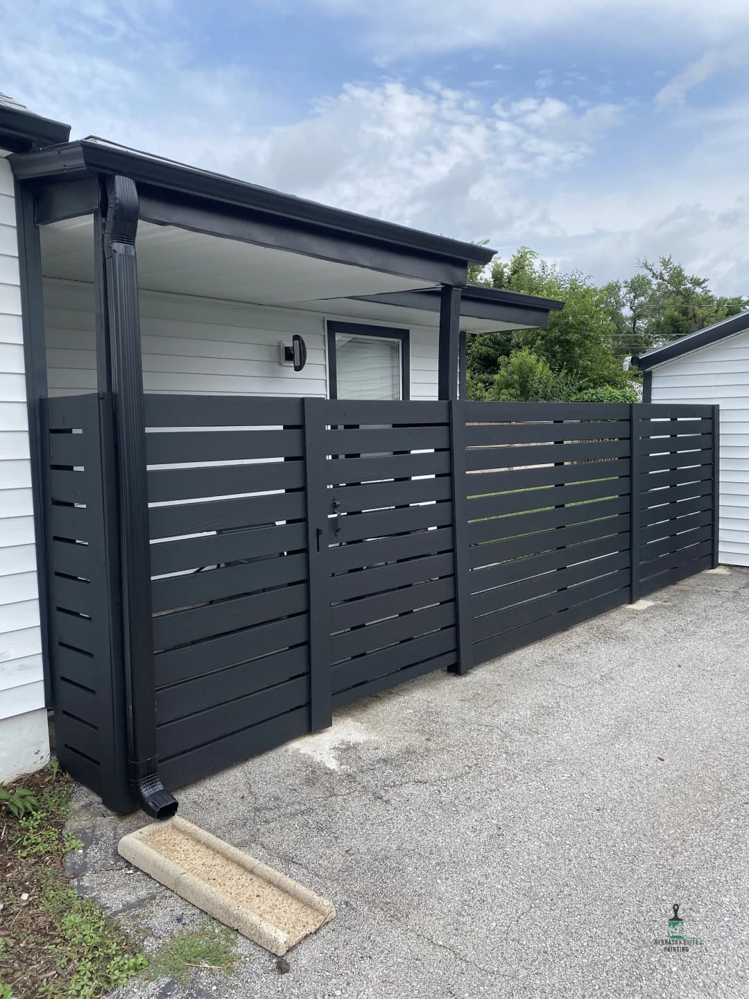 Modern black horizontal slat fence beside white house, enhancing outdoor privacy and style.