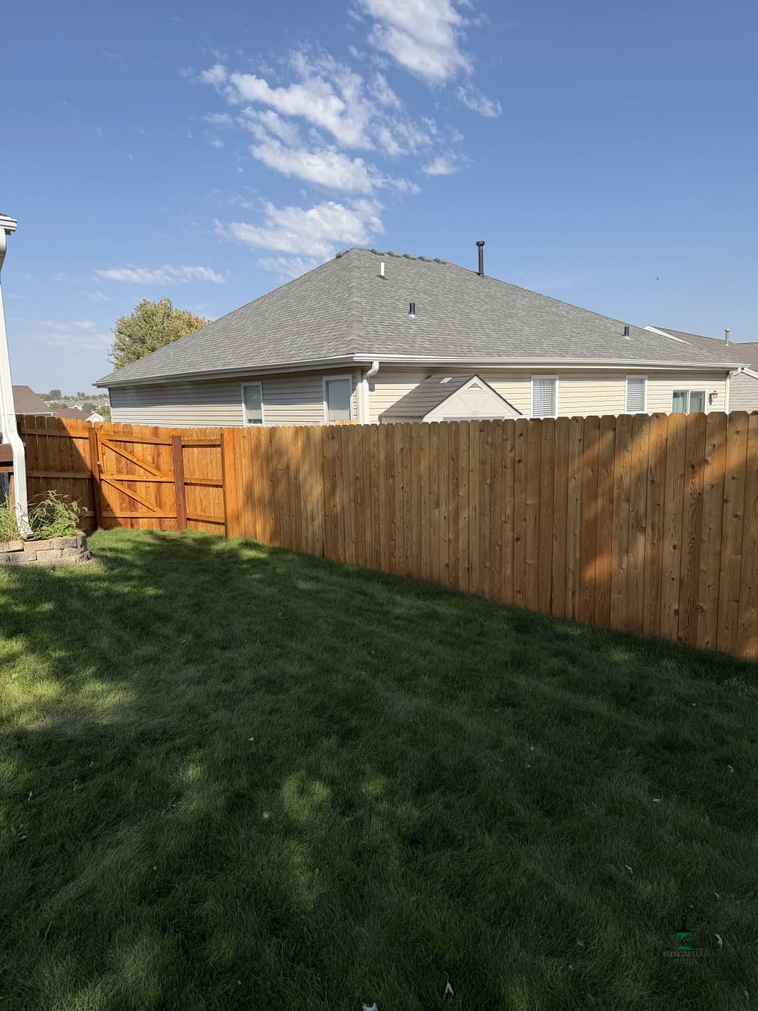 Backyard view featuring a green lawn and a wooden fence under a blue sky.