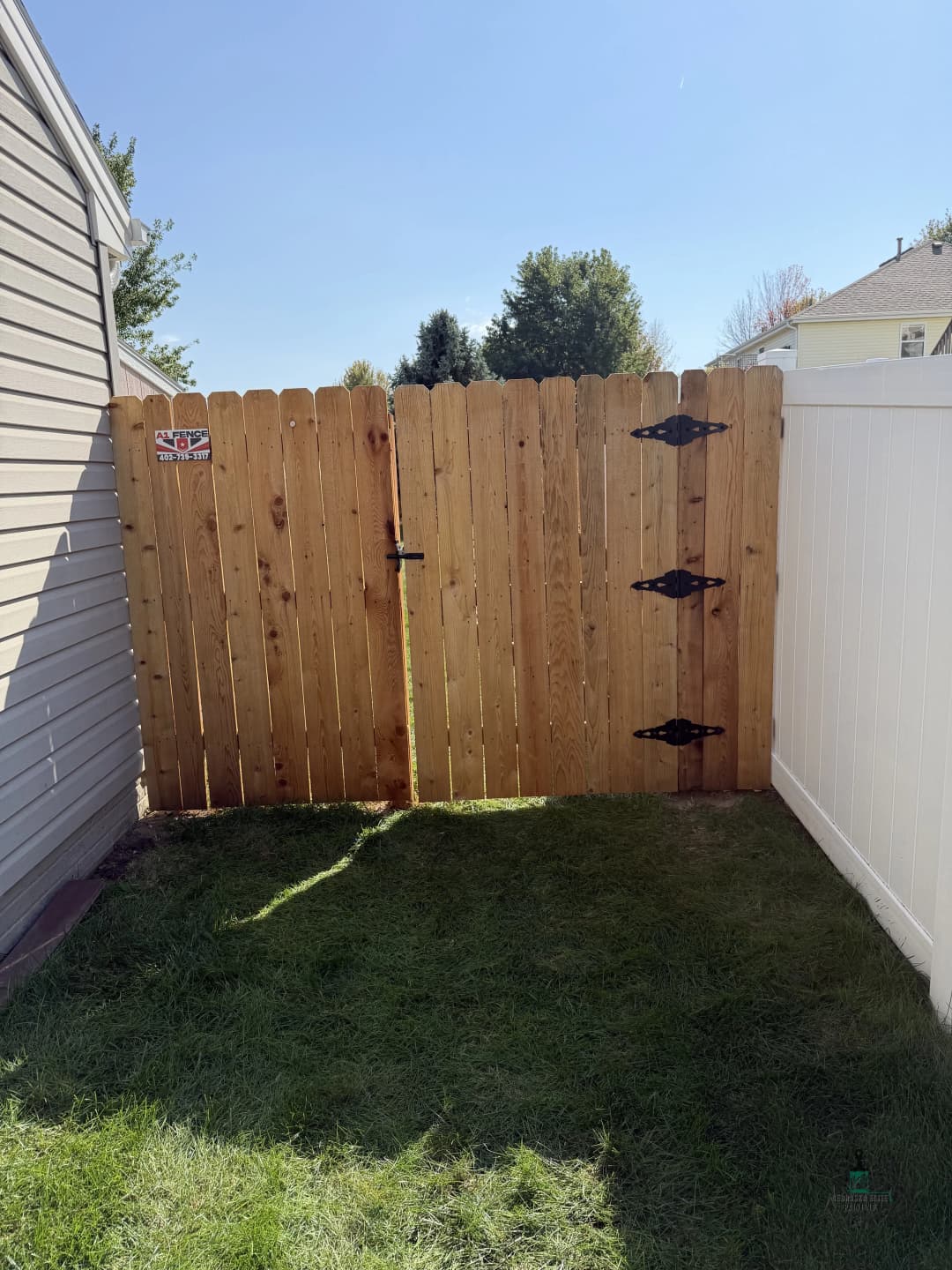 Wooden garden gate with decorative hinges, surrounded by green grass and clear blue sky.