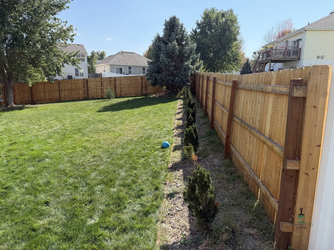 Backyard with green grass, wooden fence, and neatly aligned shrubs along the property line.