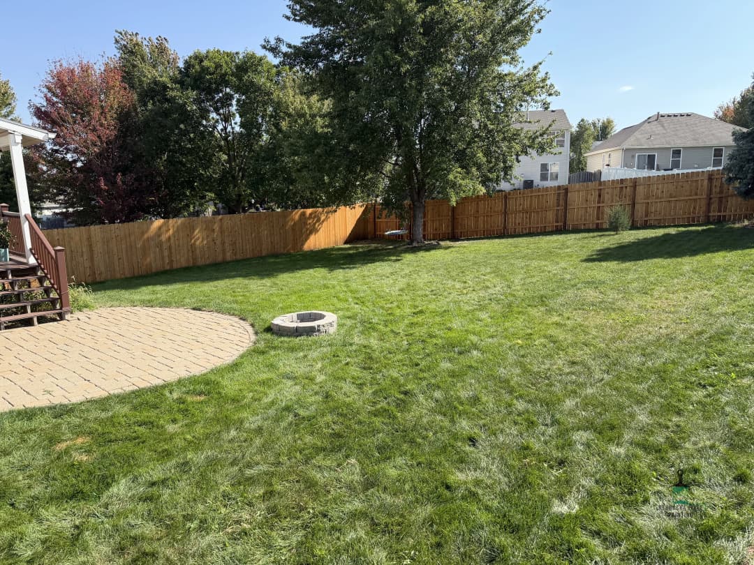 Lush green backyard with fire pit, wooden fence, and deck on a sunny day.