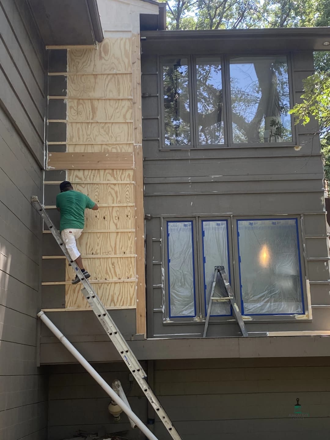 Worker installing plywood sheathing on a home's exterior, using a ladder for access.