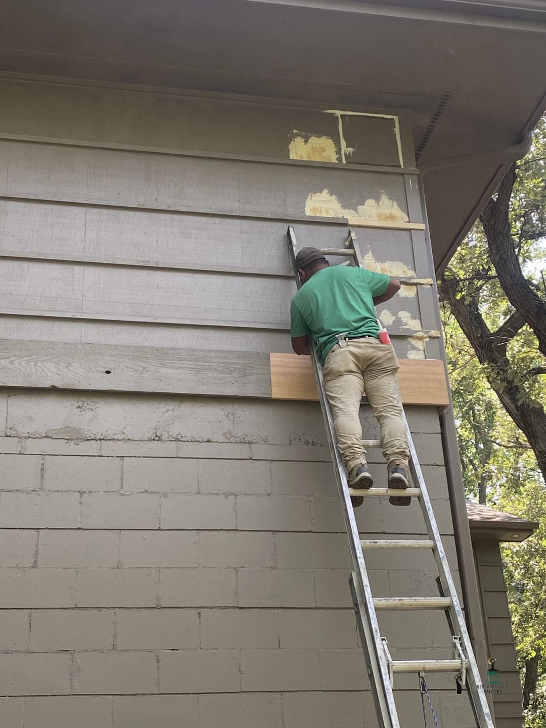 Person repairing exterior siding on a house from a ladder. Tools and materials visible.