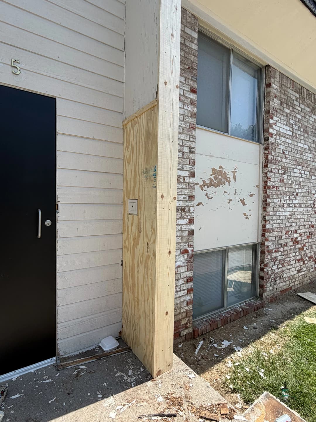Damaged exterior wall and entryway of a residential building under repair.