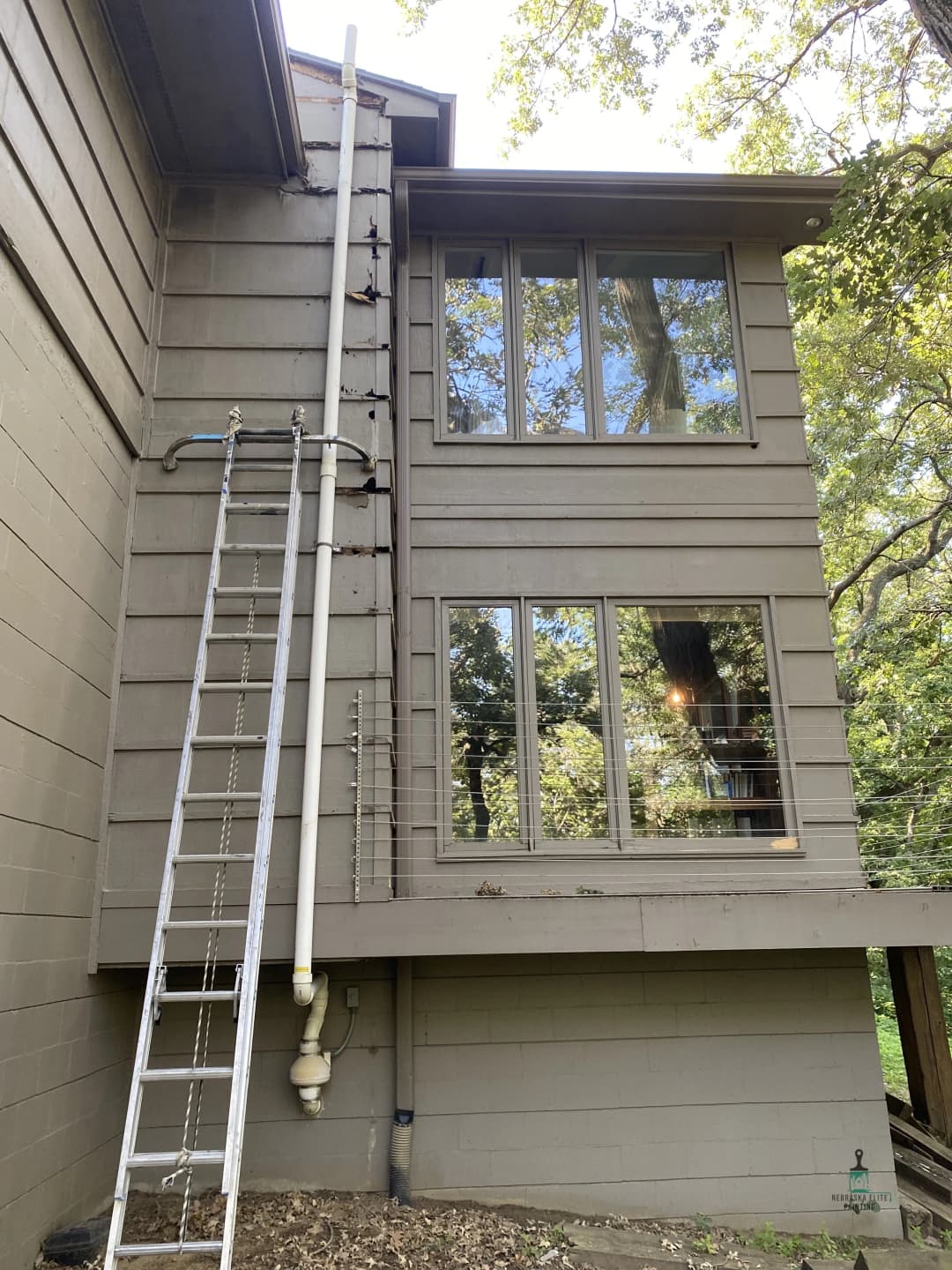 Ladder next to modern home with large windows and downspout installation.