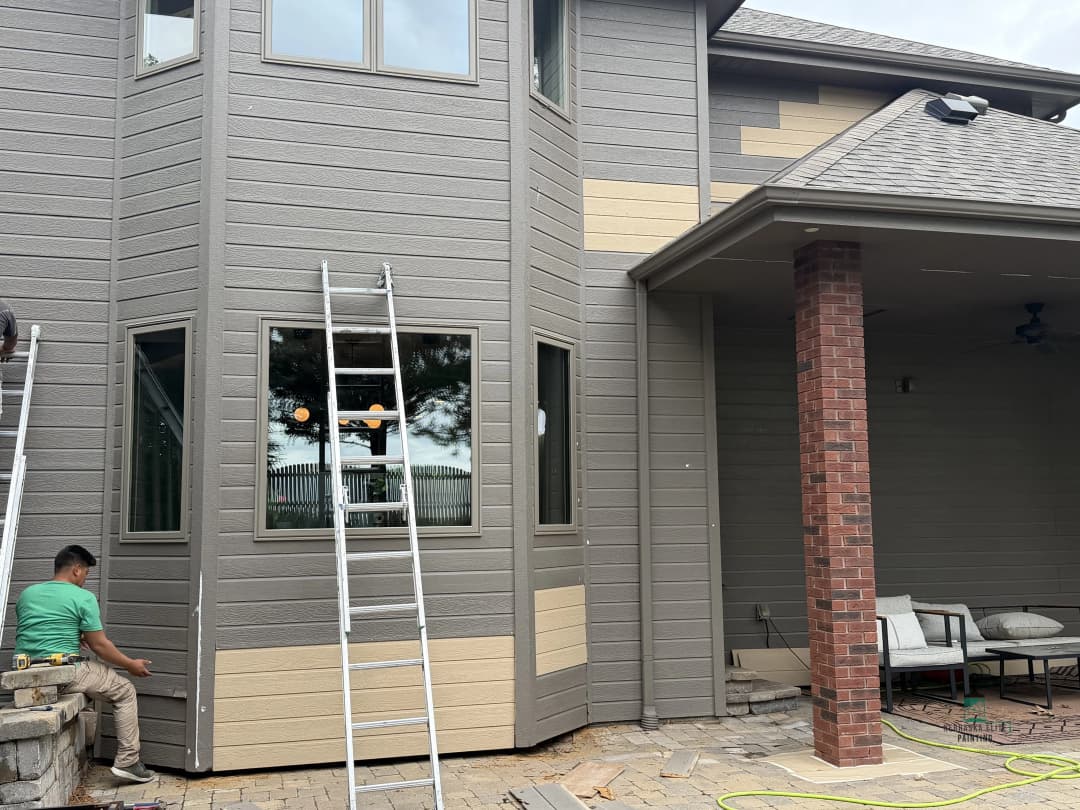 Home exterior renovation with a worker applying siding, ladder, and outdoor seating visible.