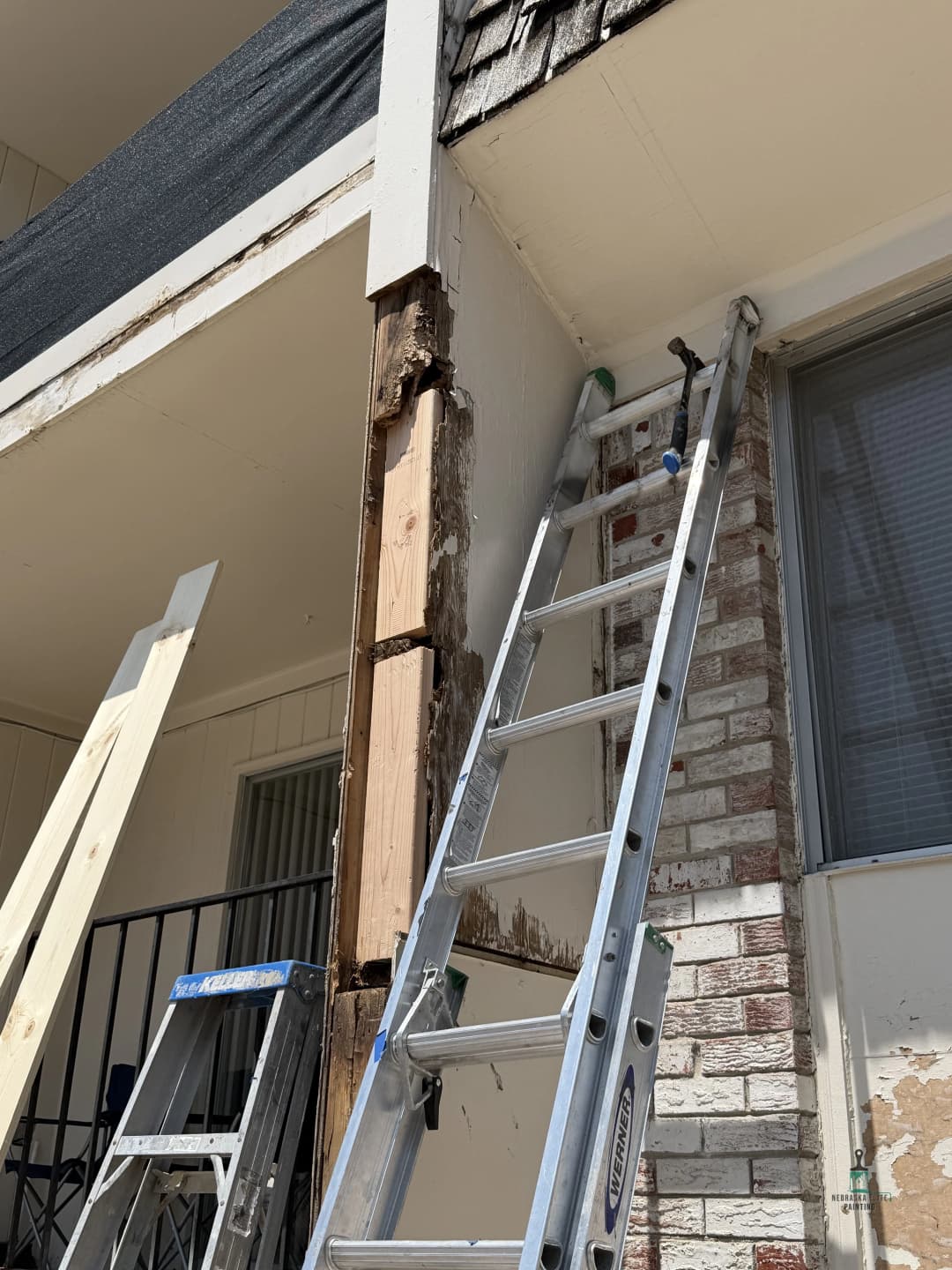 Repairing exterior damage on building with a ladder and wooden support structure.