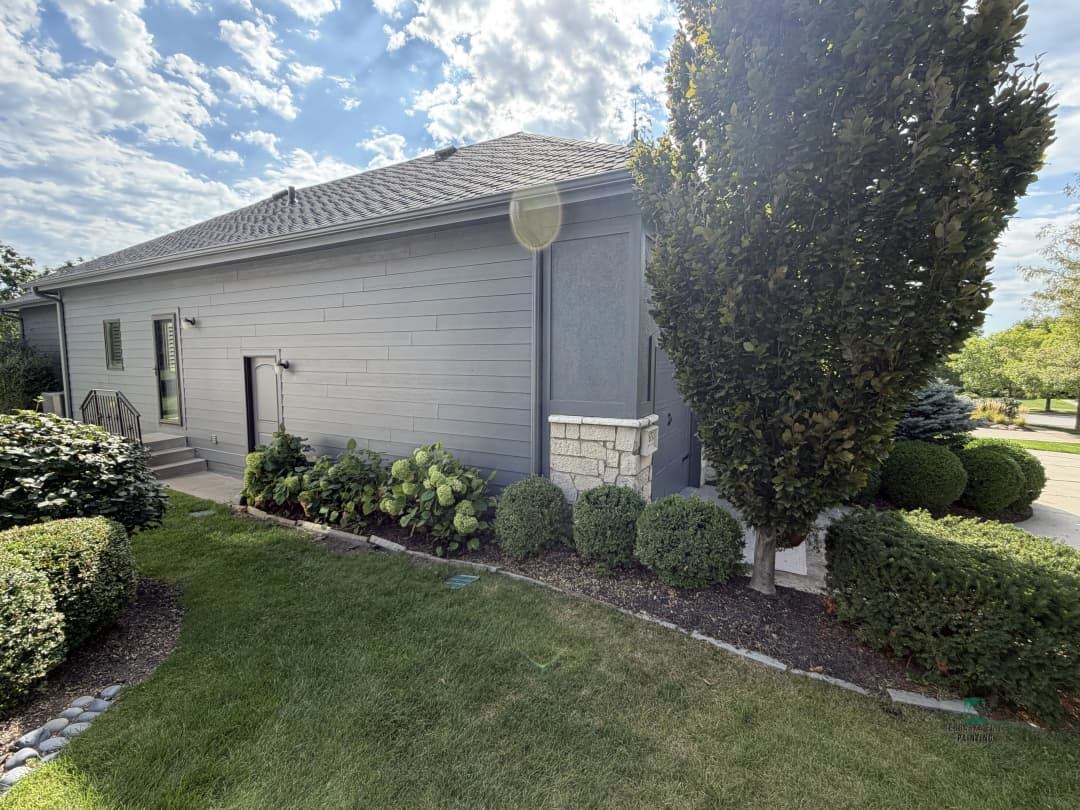 Modern gray house exterior with landscaped garden and manicured shrubs under a cloudy sky.
