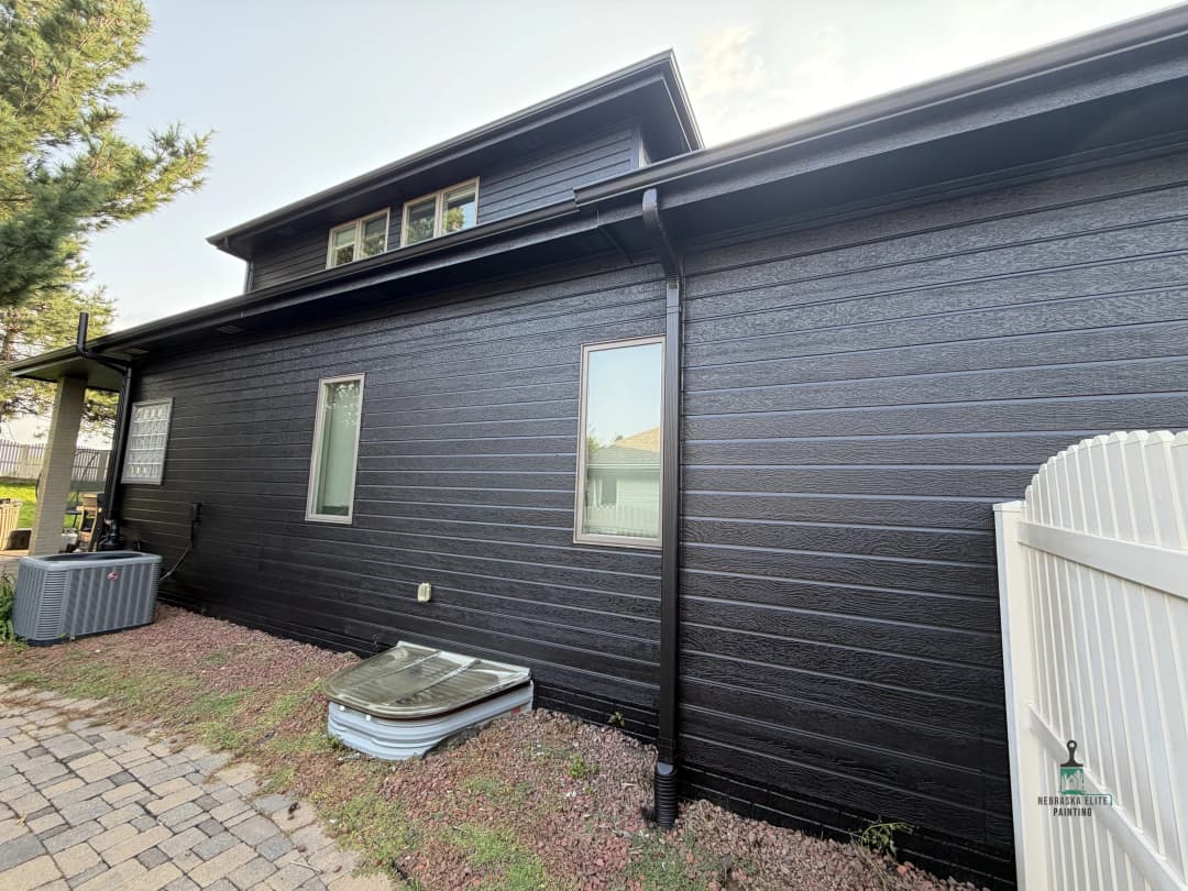 Black modern house exterior with siding, air conditioning unit, and paved pathway.