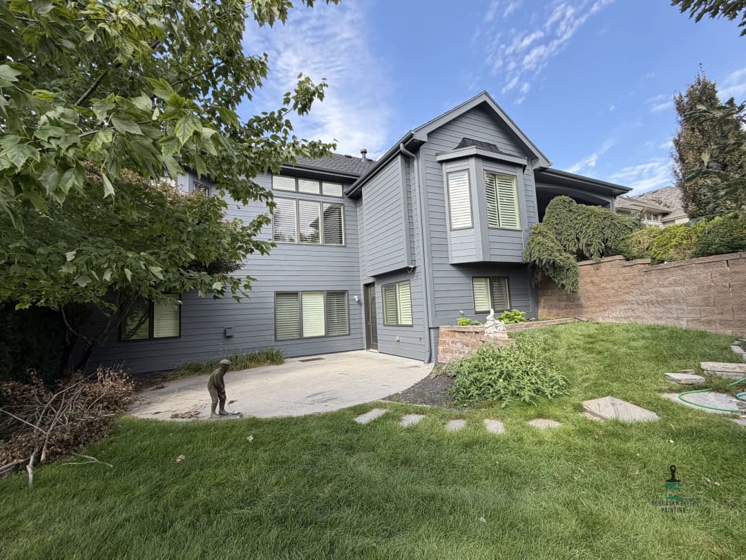 Modern gray house with green shutters and landscaped yard under blue sky.