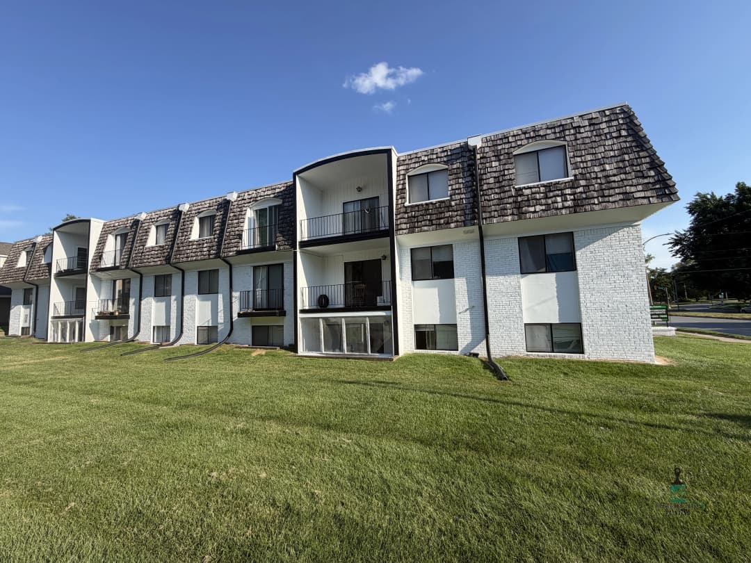 Modern apartment building with unique roof design and green lawn under a clear blue sky.