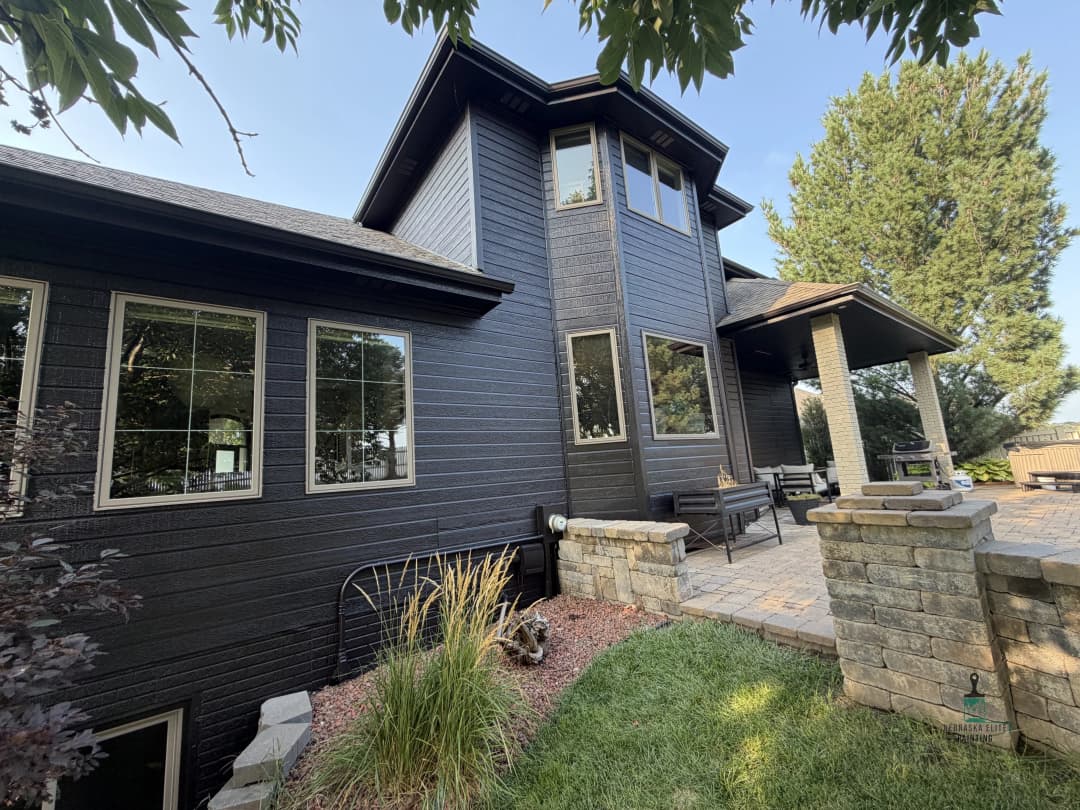Modern black exterior home with stone accents and landscaped patio area.
