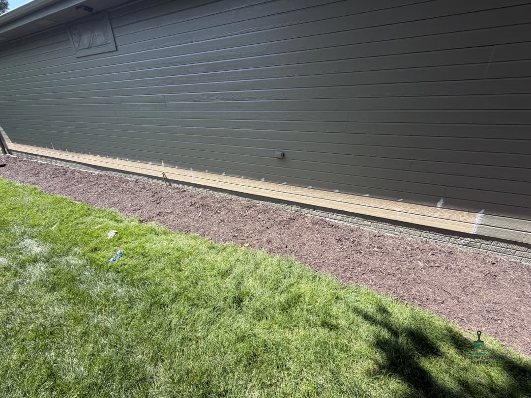 Newly installed siding on home exterior with a clean grass lawn and mulched flower bed.