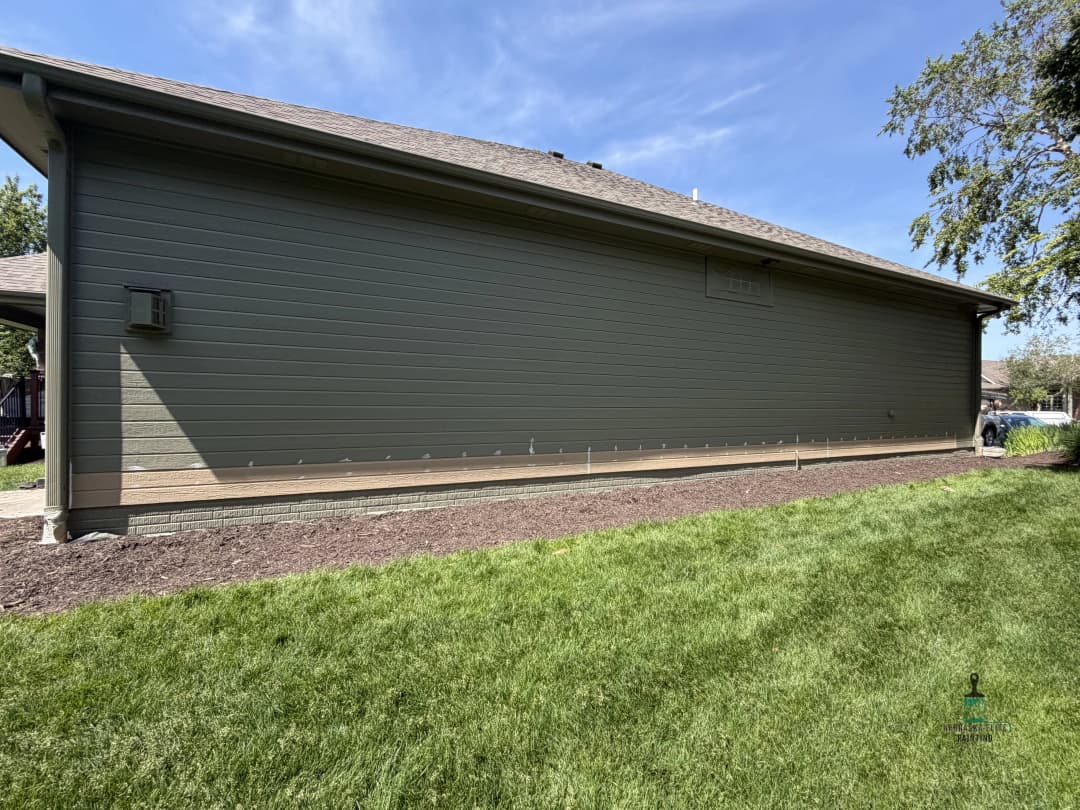 Side view of a modern home with green siding and well-maintained grass yard.