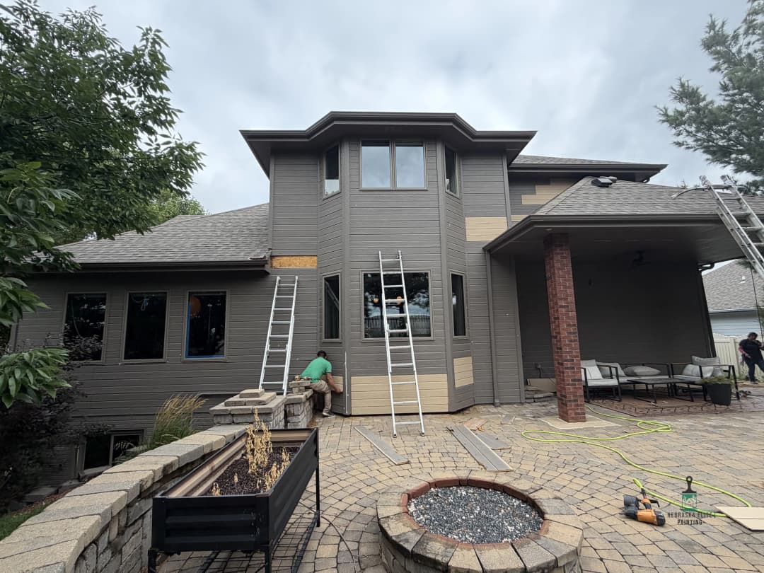 Home exterior renovation with workers, ladders, and landscaped patio area.