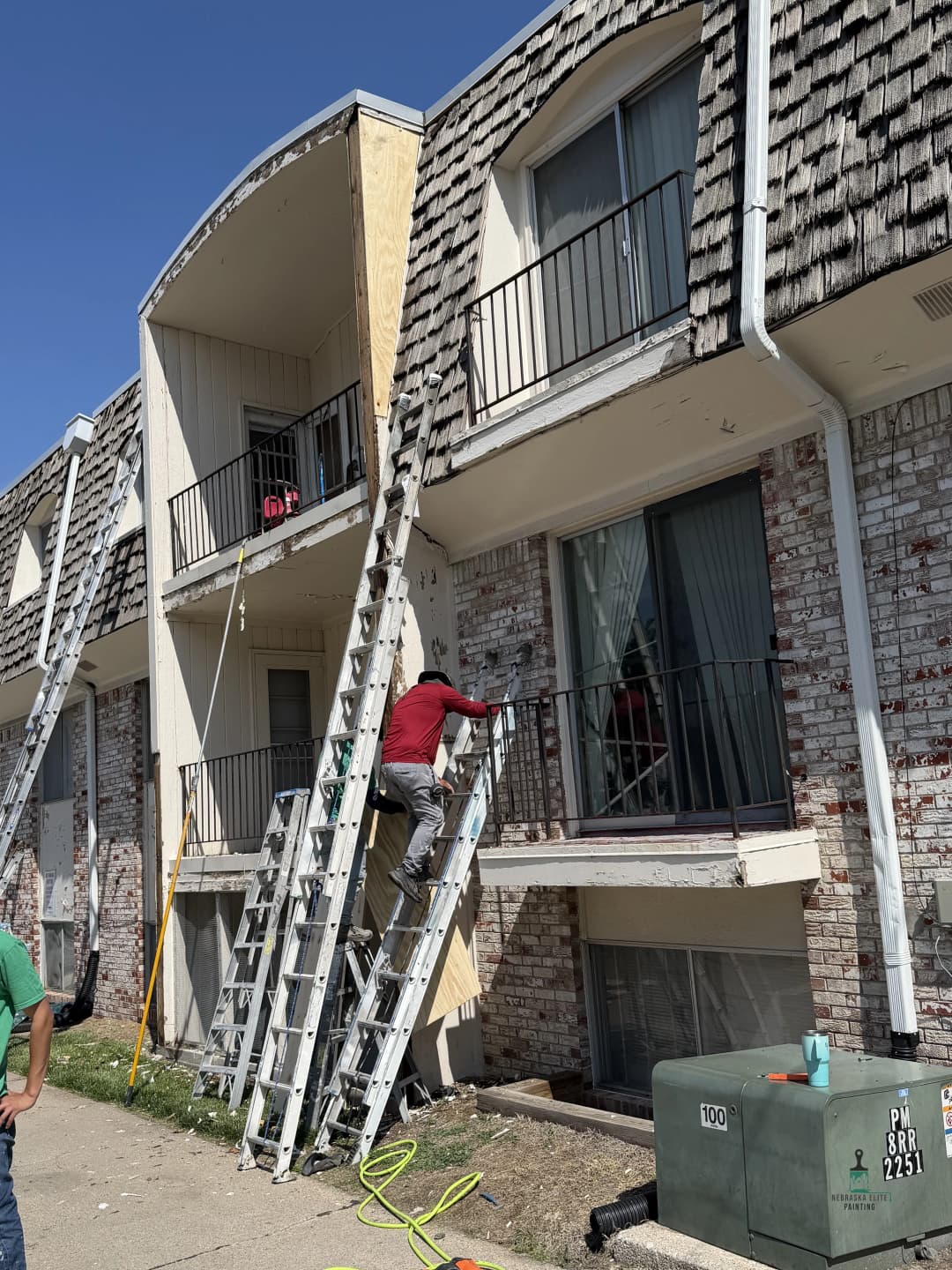 Worker on a ladder performing maintenance on an apartment building exterior.