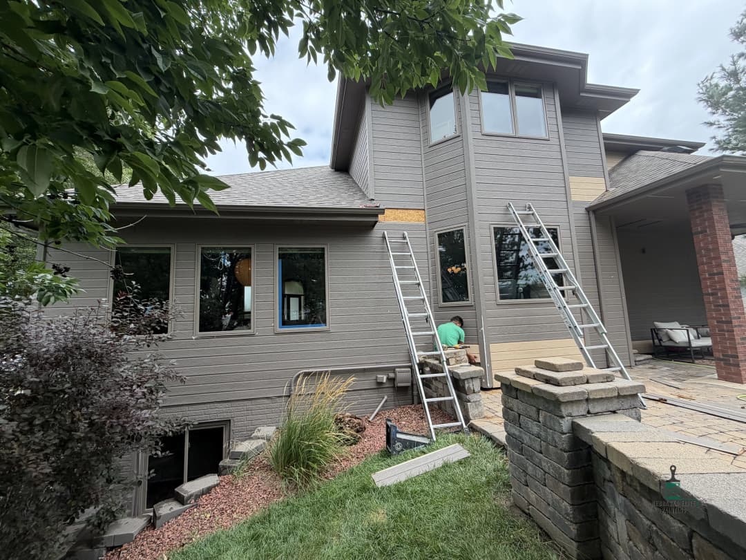 Home exterior renovation with workers, ladders, and new siding installation.